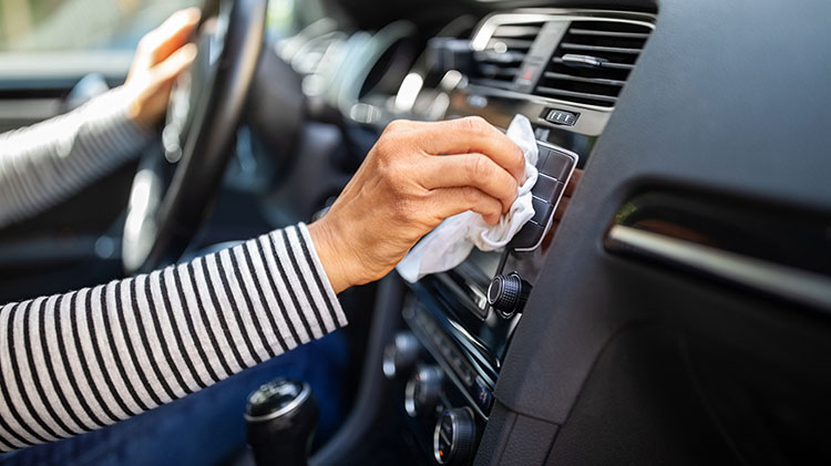 A woman wipes the vent on the dash of her car with a rag