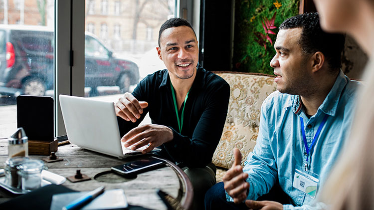 Two men talking about small business benefits and working on a laptop.