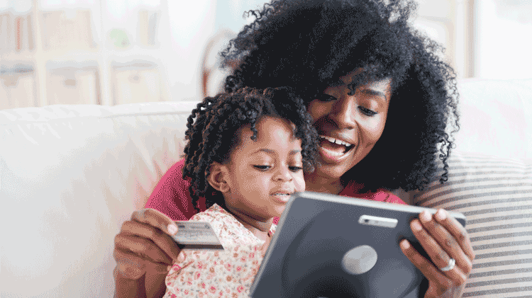 Woman reviewing balance transfer offers on her tablet with her daughter sitting in her lap