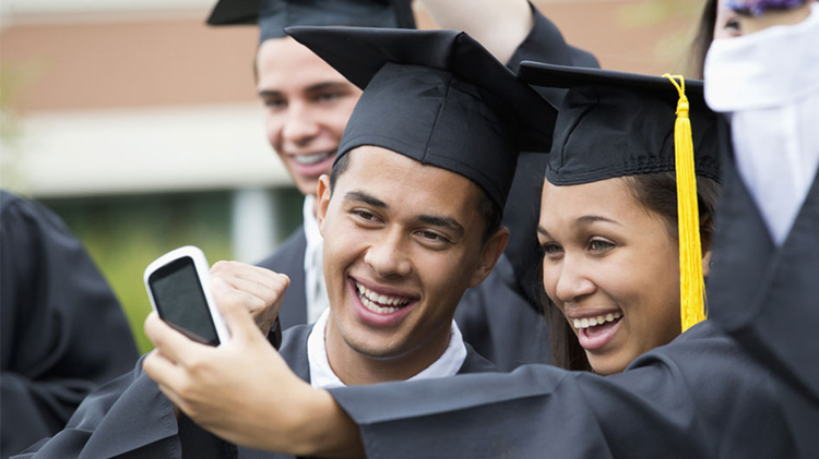 Graduates taking self-portrait together outdoors.