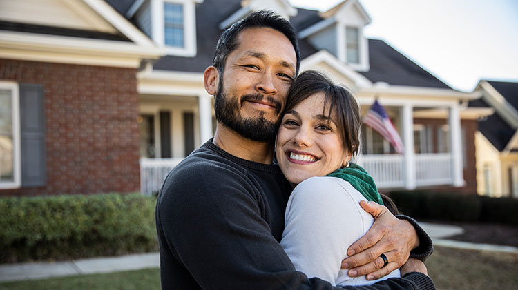 Couple hugging outside their home.