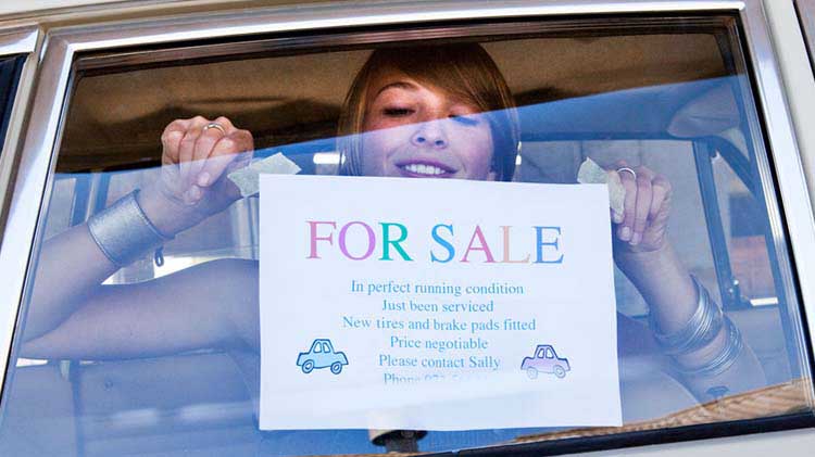 Woman hanging homemade for sale sign in car window