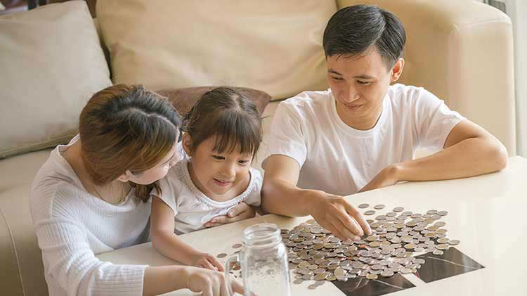 Family of three sitting around table with coins poured out from a jar.