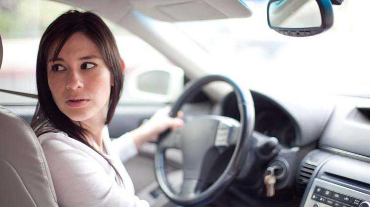 Mujer mirando detrás de ella mientras retrocede su carro.