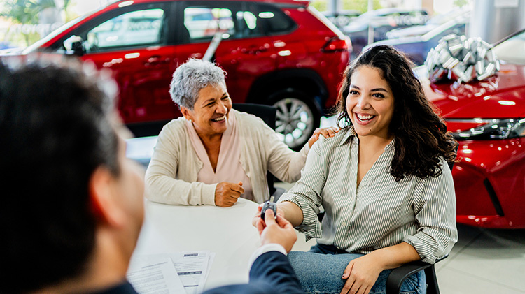 Mother and daughter receive car key for their leased vehicle at a dealership.
