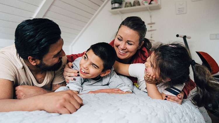 A family with a special needs child is laying on a bed talking and laughing.