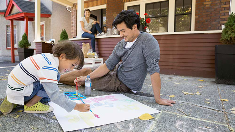 Child painting on the driveway with Dad while Mom watches from the front porch.
