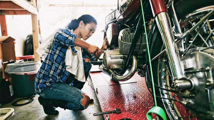 Woman kneeling down tuning up her motorcycle in a garage.