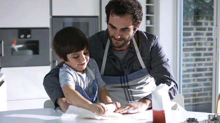 Man rolling dough with his child.