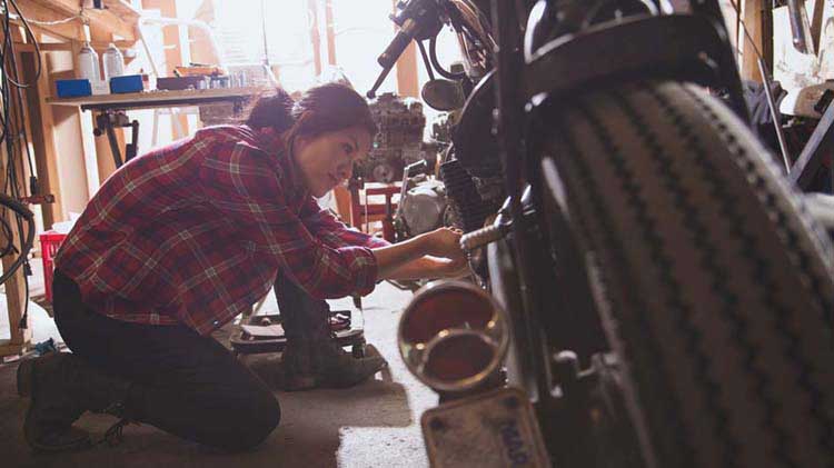 Woman kneeling down working on her motorcycle in a garage.