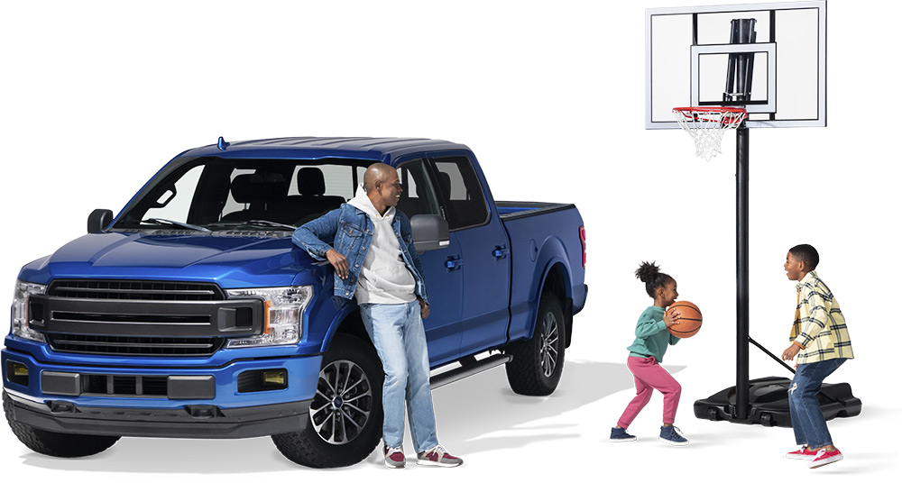 Dad leaning against blue truck watching kids play basketball