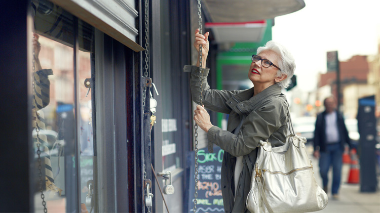 Woman closing a roller shutter to help secure her small business.