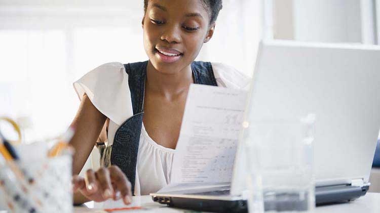 Woman searches through paperwork and on her laptop for a new apartment.