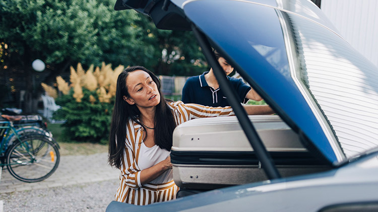 Woman with long hair takes luggage out of her car.