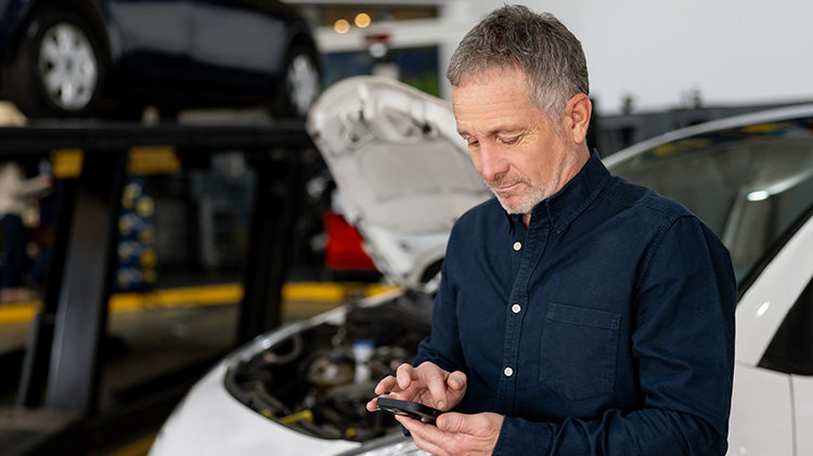 Man texts on phone at an autobody shop
