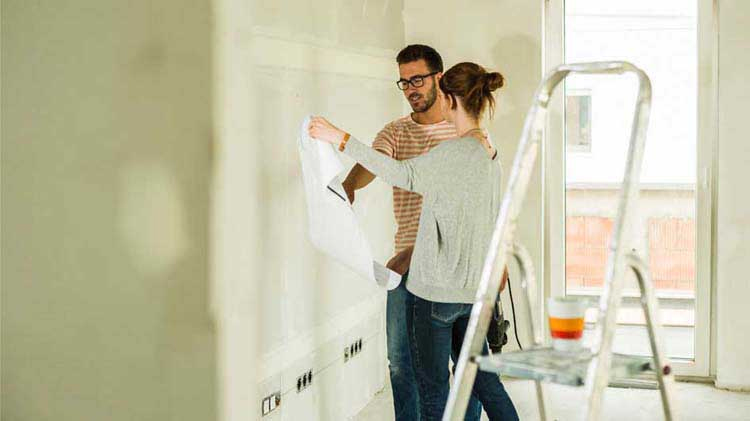 Man and woman looking at blueprints with a ladder in the foreground.