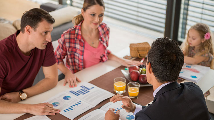 Couple discussing whether to pay for college or save for retirement with financial advisor, while daughter colors at the table.