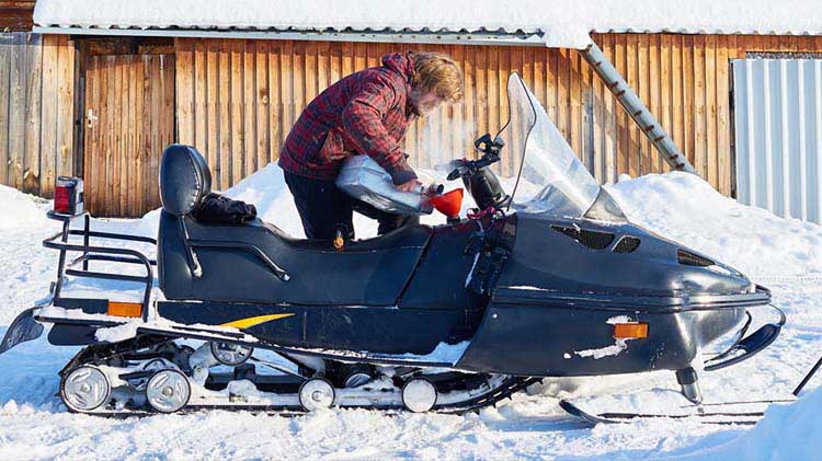 Man standing outside, adding fuel to his snowmobile.