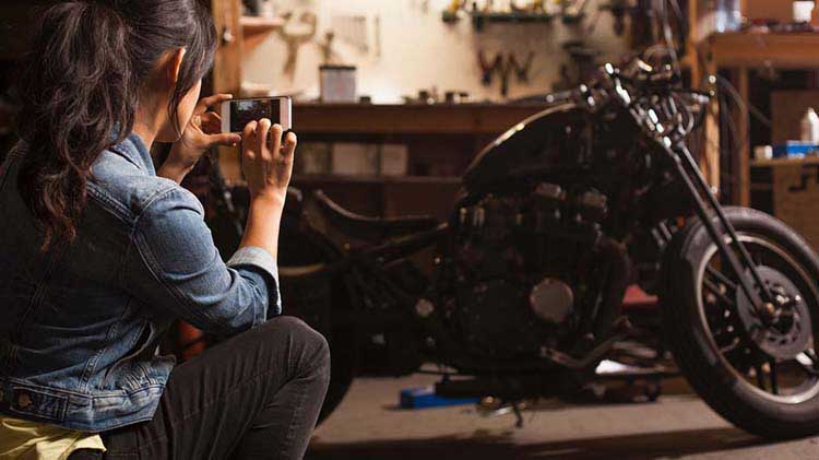 Woman taking a photo of her motorcycle with her phone.