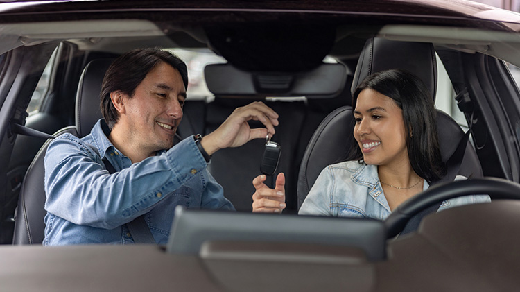 Father giving his daughter the car keys in a car they share driving.
