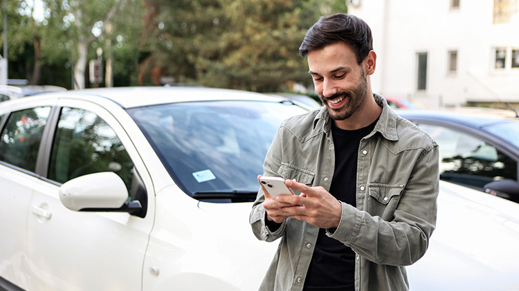 Driver standing by his car reviewing his insurance ID card in his mobile app.