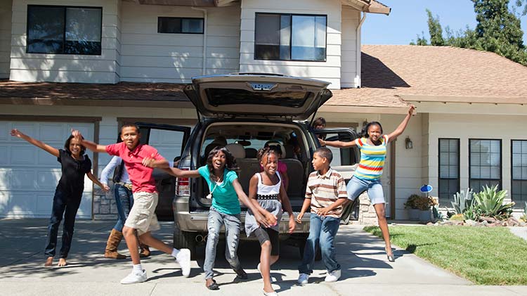 Six children are jumping with excitement outside in front of an SUV with the back hatch open.