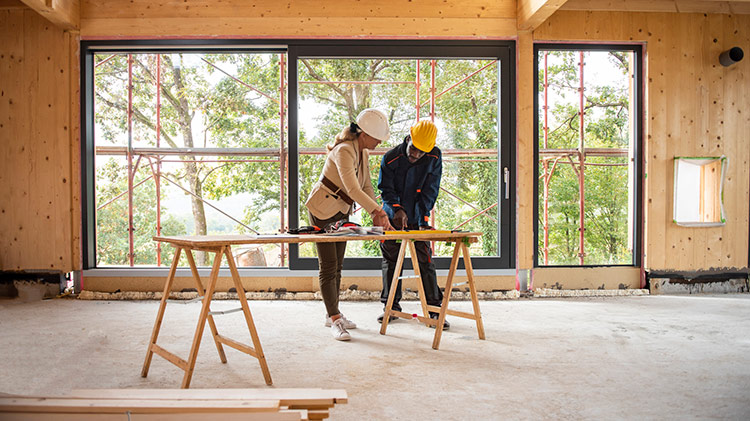 Man and woman in hardhats review construction plans indoors at a worksite.