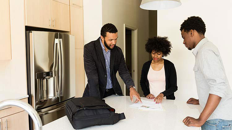 A couple and their realtor standing in the kitchen of a rental house looking at papers on the island.