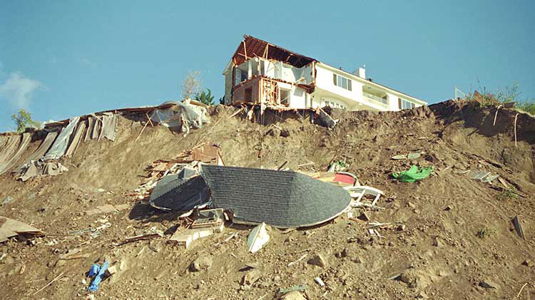A house damaged by an earthquake sits atop a hill that is covered in debris.