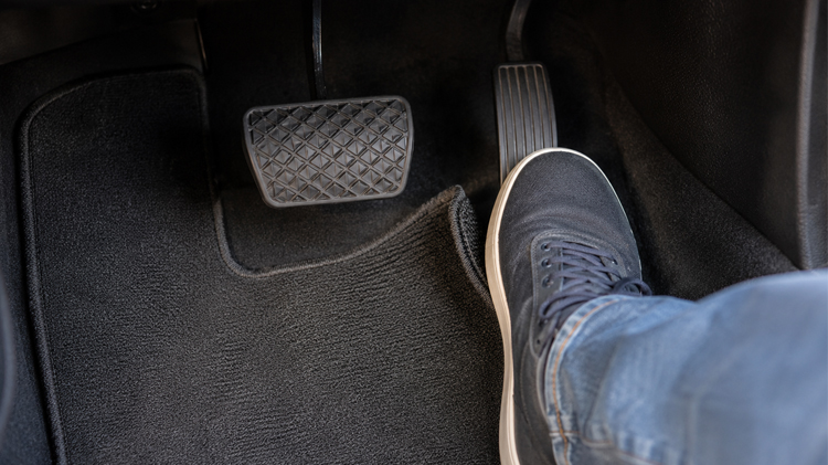 Driver’s foot near the brake and gas pedal in a car footwell.