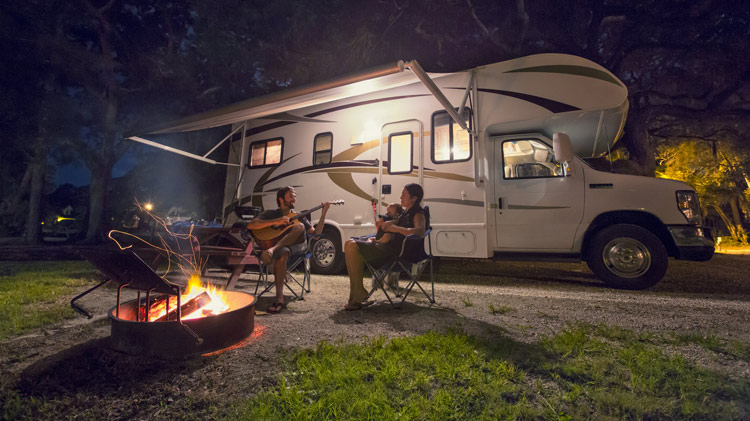 Family sitting around a campfire outside their RV.