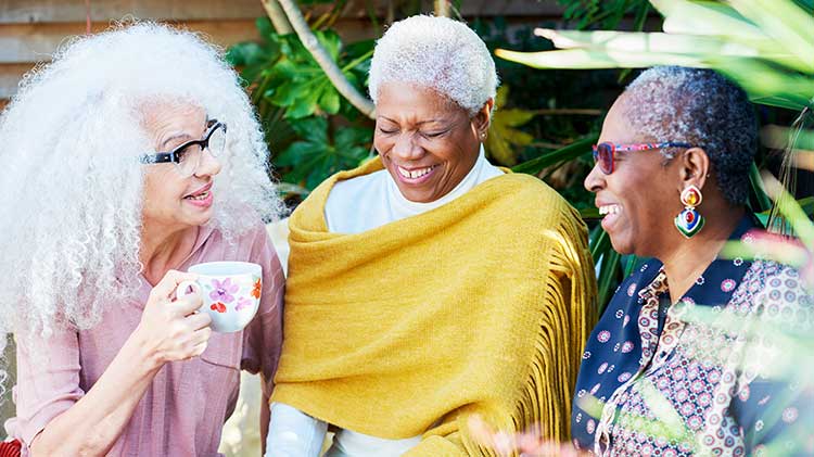 Three women laughing while discussing their retirement and sitting out side drinking coffee.