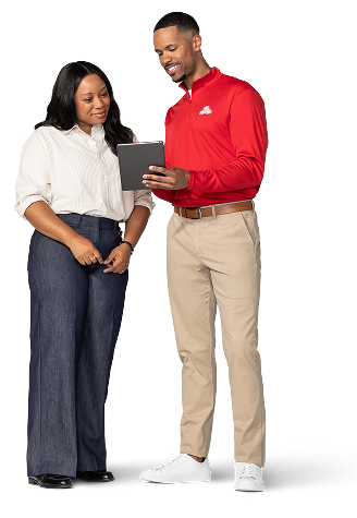 Una joven afroamericana con blusa blanca y pantalones oscuros mira la tableta que sujeta un agente joven y afroamericano de State Farm con camisa roja, pantalones caqui y tenis blancos.