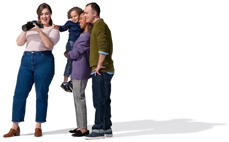 Una fotógrafa joven, caucásica y de cabello oscuro, vestida con una blusa rosa, jeans y zapatos marrones, sostiene su cámara para que la pareja con un niño pequeño pueda ver las imágenes que tomó.