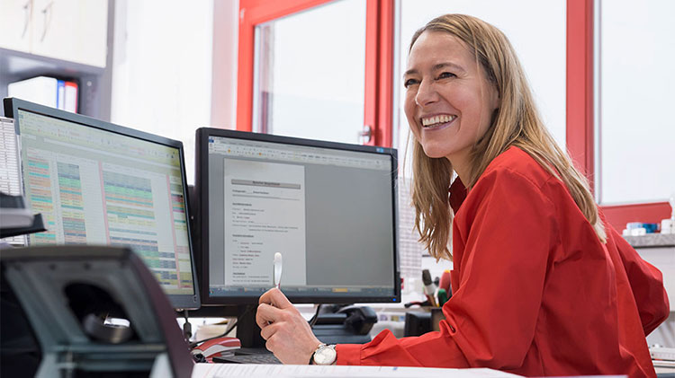 Una agente de seguros sonríe sentada en su escritorio, junto a una computadora.
