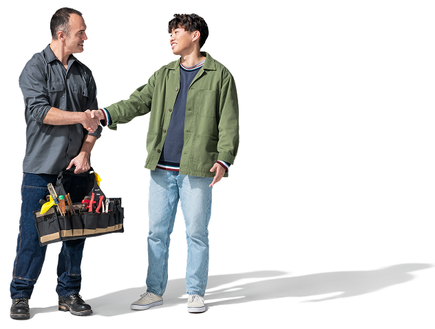 Un trabajador de raza blanca con camisa gris oscuro, pantalones azul marino y botas de trabajo sostiene una bolsa de herramientas y estrecha la mano de un joven asiático con chaqueta verde oliva, sudadera azul, jeans y tenis blancos.