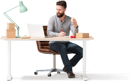 An investor in grey shirt and jeans sits behind a desk. He’s holding a small candle and checking inventory on his laptop.
