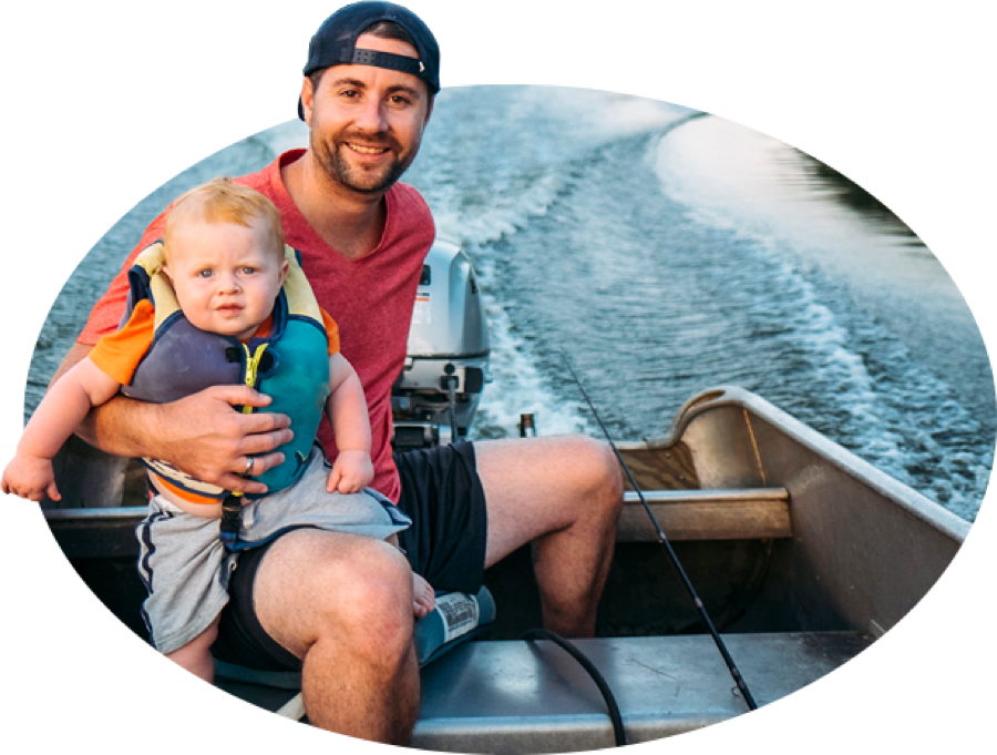 Un joven padre barbado y su pequeño hijo portando chaleco salvavidas navegan en una embarcación de pesca, una de las muchas clases cubiertas por el seguro de embarcaciones de State Farm.