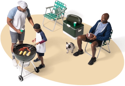 View from above of a father and son grilling hotdogs and corn on the cob as a neighbor and his dog supervise from a nearby lawn chair.