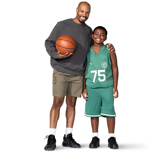 ”Holding a basketball, a father has his other arm draped around his son’s shoulders. His son is wearing a basketball uniform.