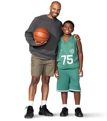 ”Holding a basketball, a father has his other arm draped around his son’s shoulders. His son is wearing a basketball uniform.