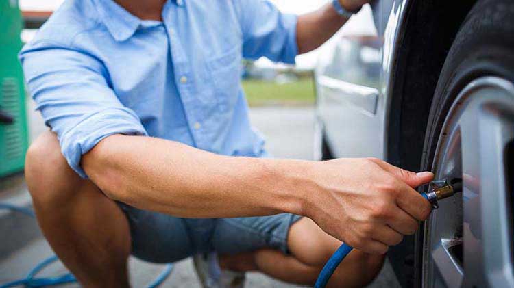 A man in a blue shirt checks his tire pressure.