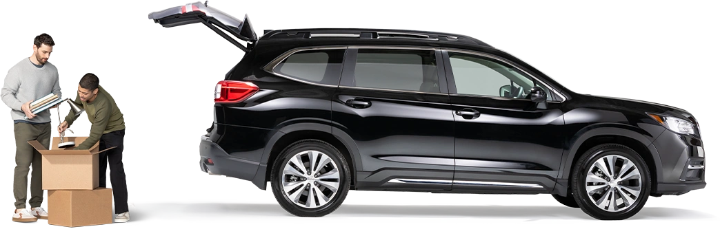 Standing behind a black SUV with open hatch, a pair of roommates pack a lamp and notebooks into a box.