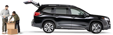 De pie detrás de un SUV negro con la cajuela abierta, un par de compañeros de cuarto empacan una lámpara y cuadernos en una caja.