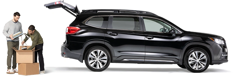 Standing behind a black SUV with open hatch, a pair of roommates pack a lamp and notebooks into a box.