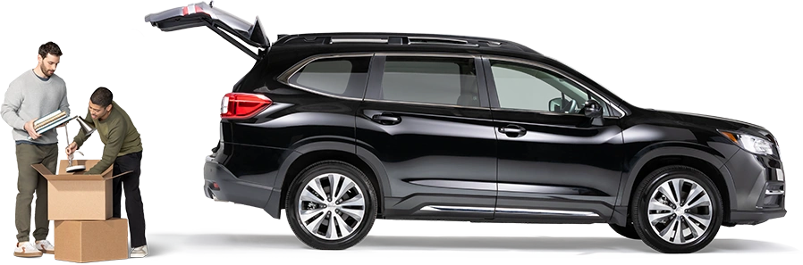 De pie detrás de un SUV negro con la cajuela abierta, un par de compañeros de cuarto empacan una lámpara y cuadernos en una caja.