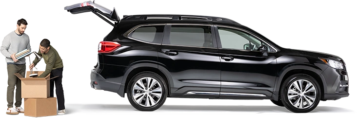 De pie detrás de un SUV negro con la cajuela abierta, un par de compañeros de cuarto empacan una lámpara y cuadernos en una caja.