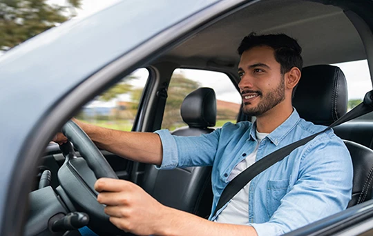 Un conductor con una camisa azul sonríe con su cinturón de seguridad abrochado.