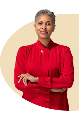 Con los brazos cruzados, una agente mayor de State Farm con blusa y bufanda rojas sonríe.