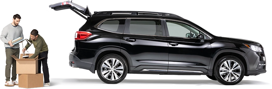 Standing behind a black SUV with open hatch, a pair of roommates pack a lamp and notebooks into a box